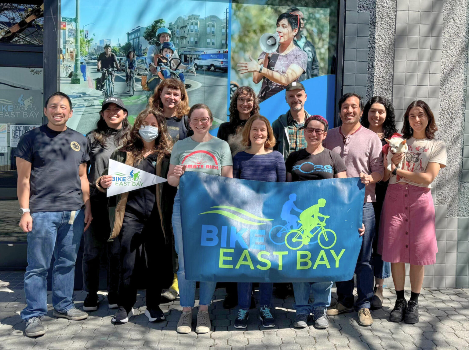 The Bike East Bay staff stands outside of the office, holding a banner with their logo. Smiling faces!
