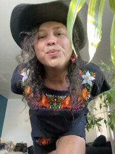 Francisco is leaning towards the camera, wearing a cowboy hat, black shirt with embroidered flowers, and beaded earrings.