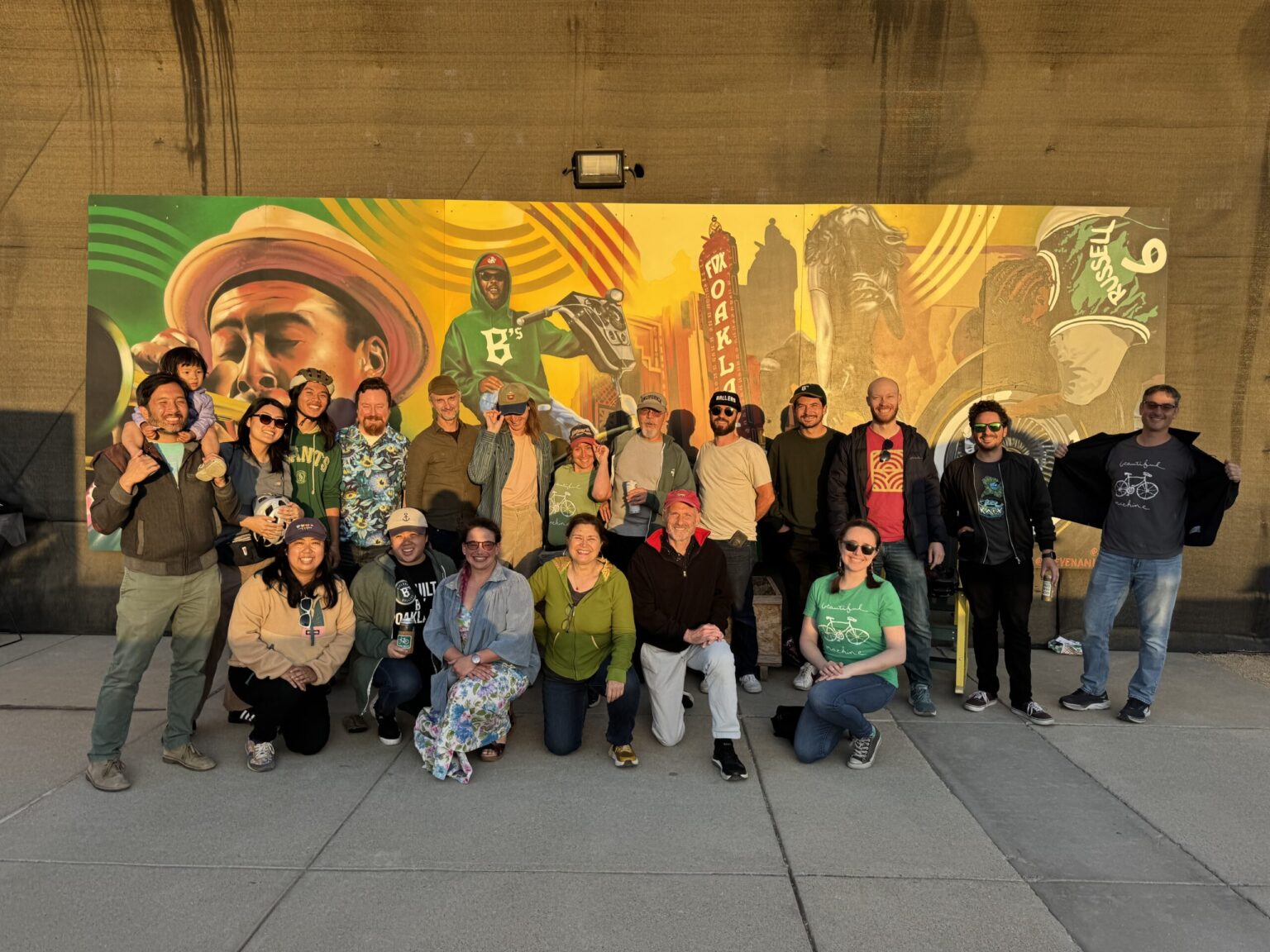 A diverse group of 20ish people of smiling for a group photo, in front of a mural at a Ballers baseball game