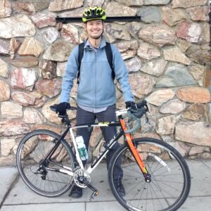 Jianhan is standing behind their road bike, smiling in everyday clothes and a neon helmet.