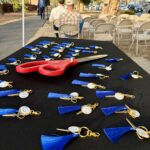 Photo of a table set up behind rows of chairs along a paved multi-use trail. A large pair of ceremonial scissors is placed on the table, along with many small keychains with scissor charms
